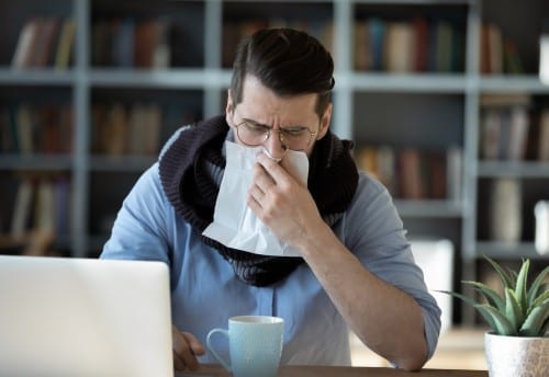 Sick businessman blowing running nose, sitting at work desk