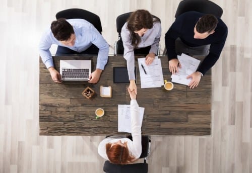 overhead view of panel job interview with interviewee shaking hands with one of the panel