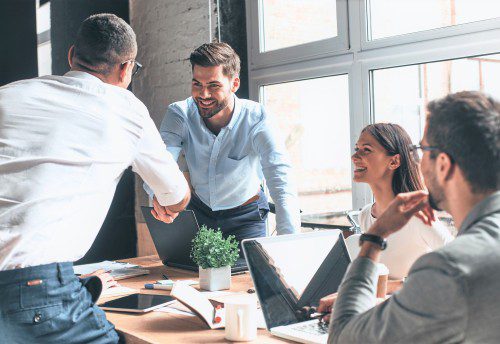 Business advisors around a table with two shaking hands and smiling