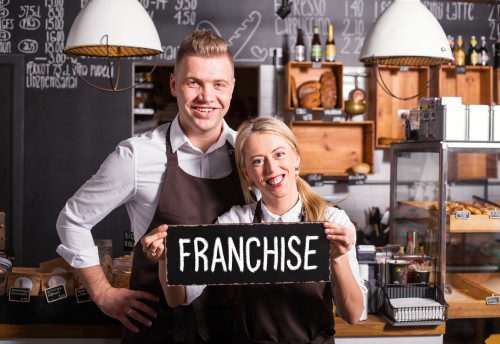 Woman and man smiling with a blackboard franchise sign