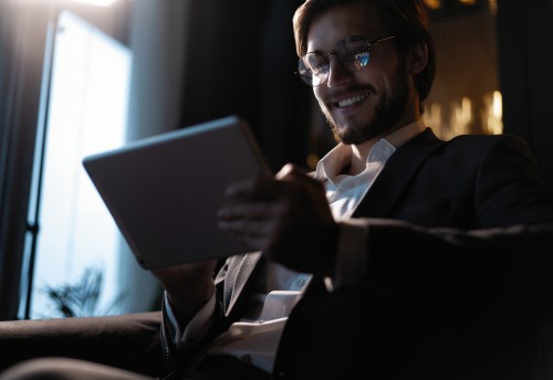 smiling Businessman working using tablet computer while sitting in cafe late at night in front of windows