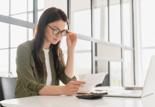 Successful young female with glasses accountant using calculator in office.