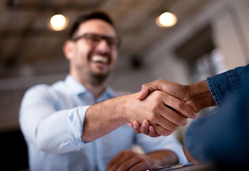 two business men shaking hands, one smiling blurry with glasses