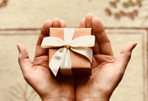 Small square wooden gift box with a white ribbon in the palm of two hands together