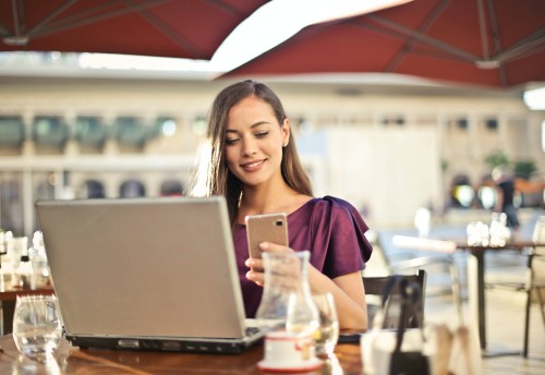 young woman on her phone infront of a laptop