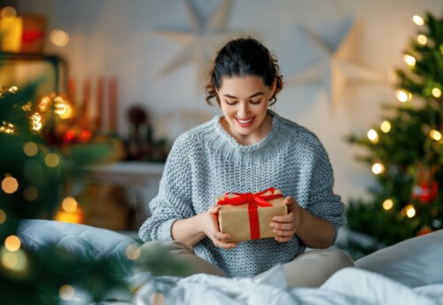 women in cosy jumper looks smiling at a Christmas present with a red bow
