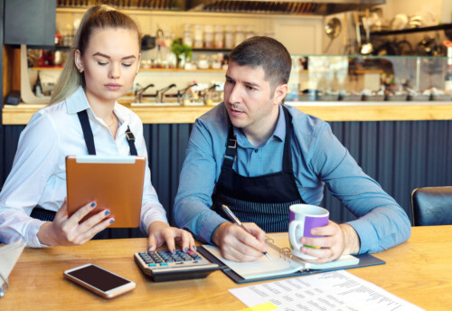 Small family restaurant owners discussing finance calculating bills and expenses of new small business - Stressed man and woman going through paperwork together in coffee shop